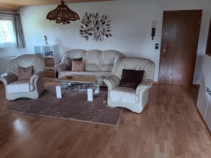 A living room with a sofa, two armchairs, a coffee table, a wall-mounted decorative piece, and a wooden door. - Apartment 'Schupp' with Mountain View, Shared Terrace and Wi-Fi (Dachsberg (Südschwarzwald))