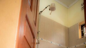 Une salle de bain avec une porte en bois, des toilettes, une douche avec un pommeau de douche amovible et un porte-serviettes.