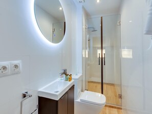 Un baño moderno con cabina de ducha de vidrio, un lavabo blanco y un inodoro.