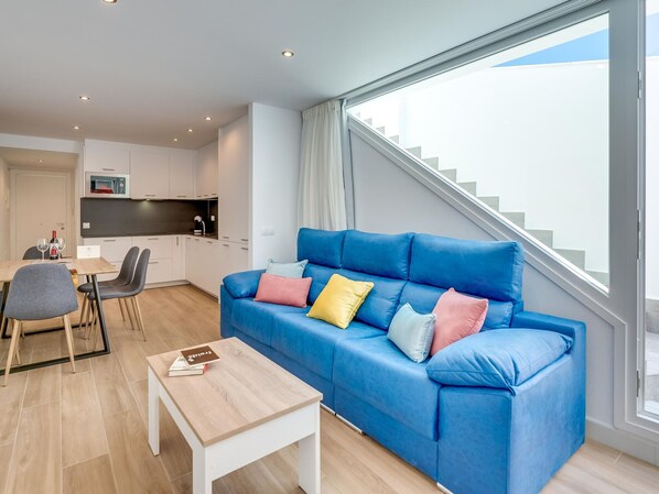 Una sala de estar moderna con un sofá azul, una mesa de comedor y una zona de cocina.