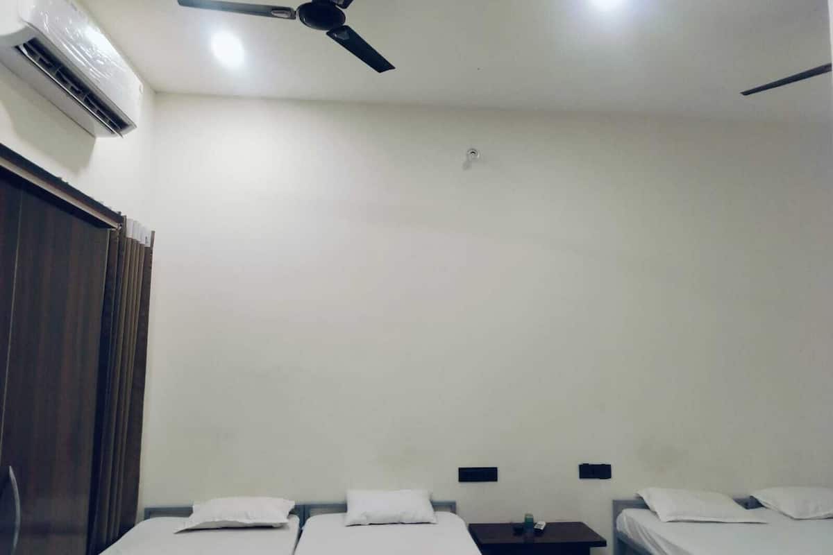A hotel room with two single beds, a ceiling fan, an air conditioning unit, and a wooden wardrobe.