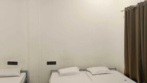 A room with two beds, a ceiling fan, an air conditioner, and a curtain. - Agralok Dham (Ujjain)