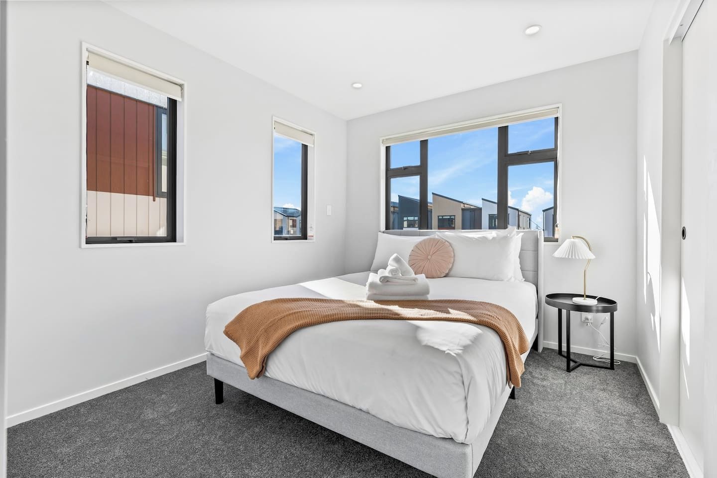 A modern hotel room with a large bed, a small bedside table, and a view of buildings outside.