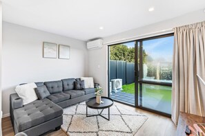A modern living room with a grey sectional sofa, a small round coffee table, and a large sliding glass door leading to a backyard.