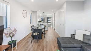 A modern living room with a grey sofa, a dining area with a round table and chairs, and a kitchen in the background.