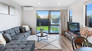 A modern living room with a grey sofa, a TV, and a sliding glass door leading to a garden.