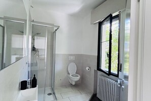 Un bagno piccolo e compatto con il water, uno spazio doccia, un lavandino e una finestra con vista sul verde.