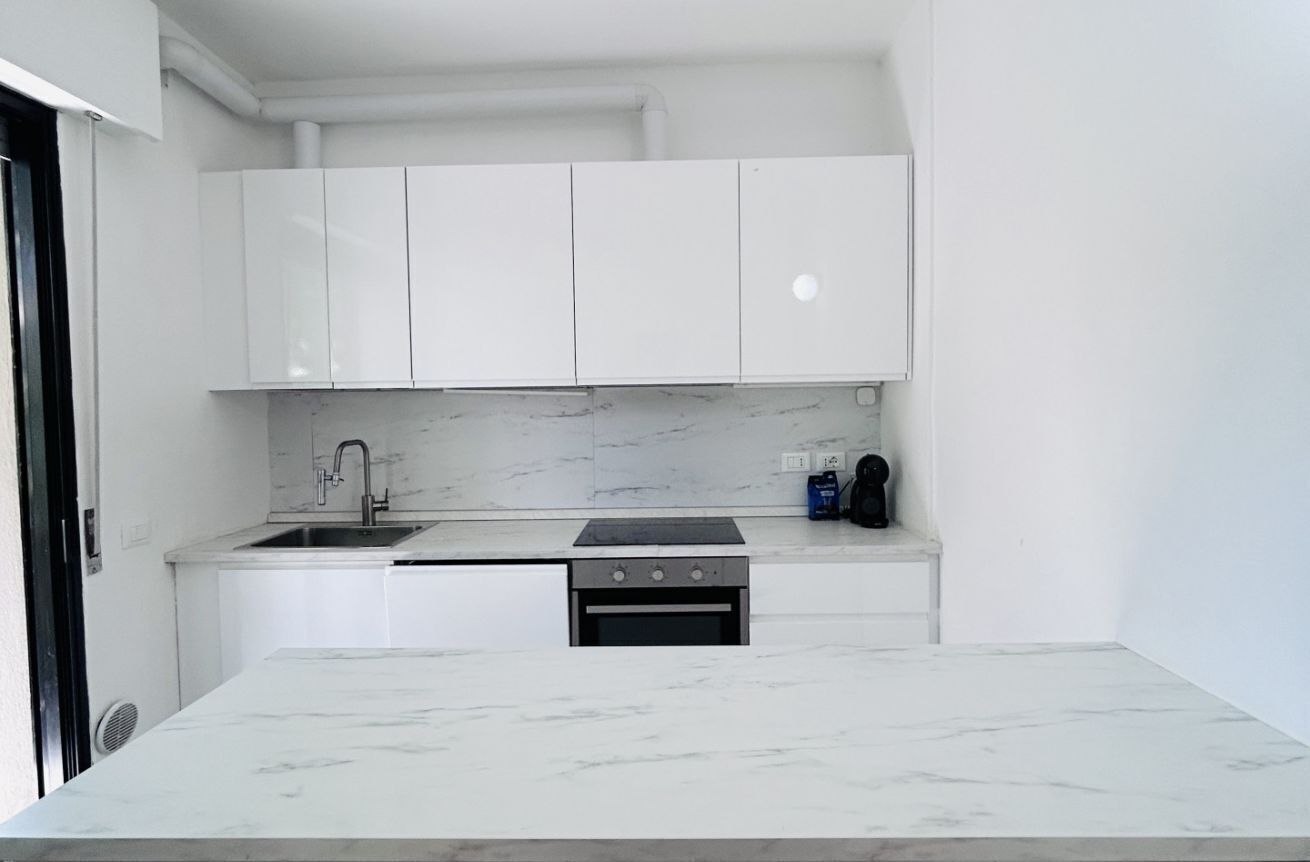 Una cocina moderna con armarios blancos, encimera de mármol, horno empotrado y un lavamanos.