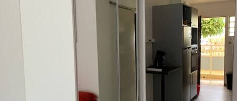 Ein modernes Zimmer mit Schiebetürenschrank, einer kleinen Küchenzeile und einem Bett mit roter Bettwäsche.