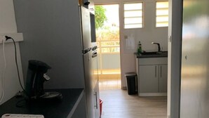 Eine schmale Küche mit schwarzem Arbeitsplatz, einer Mikrowelle und einem kleinen Spülbecken. Ein Fenster lässt natürliches Licht herein und bietet einen Ausblick nach draußen.
