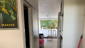 Ein Flur mit Holzboden, einem roten Mop-Eimer und einer Tür zu einem Raum mit einem roten Bett.