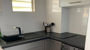 Eine kompakte Küche mit Einbauwaschmaschine, Spüle und einem Fenster mit Jalousien.