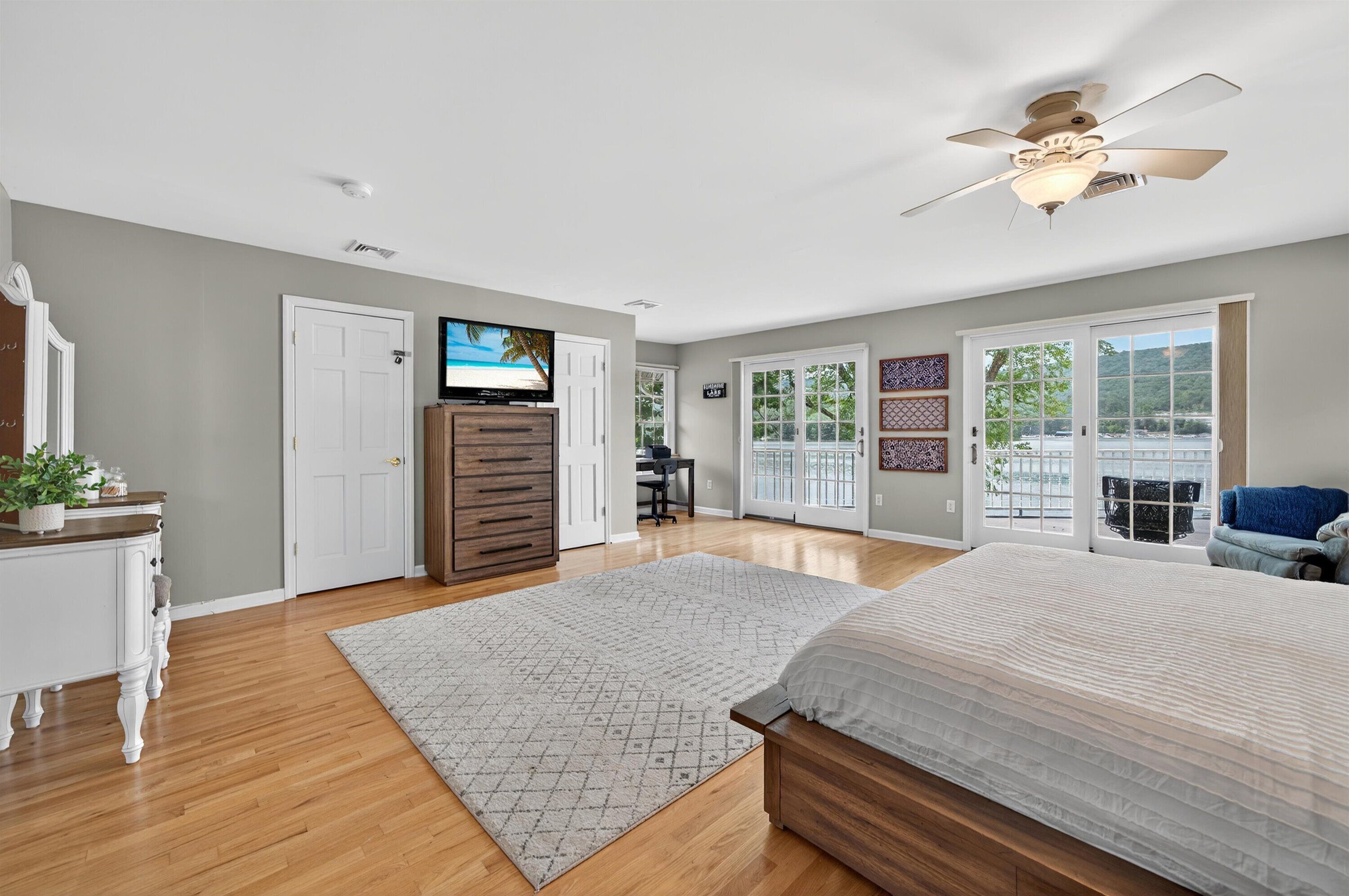 A bedroom with a bed, a dresser, a TV, and a ceiling fan.