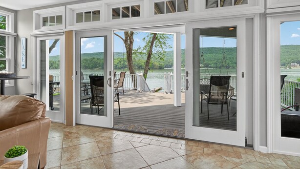 A spacious room with a large sliding glass door leading to an outdoor deck with a view of a lake and hills.