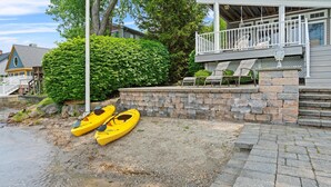 A waterfront property with a stone wall, a covered porch, and two yellow kayaks by the water.