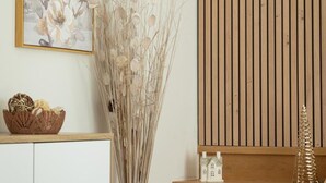 A room with a wooden slat wall, a framed floral artwork, a tall dried plant arrangement, a small white house model, and a decorative basket. - New house in Sarlat with garden and terrace (Sarlat-la-Canéda)