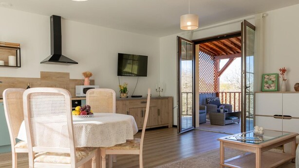 A modern living room with a dining area, wooden flooring, and a large sliding glass door leading to an outdoor patio. - New house in Sarlat with garden and terrace (Sarlat-la-Canéda)