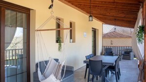 A covered patio area with a wooden ceiling, a hanging hammock, a dining table with chairs, and a view through a glass door. - New house in Sarlat with garden and terrace (Sarlat-la-Canéda)