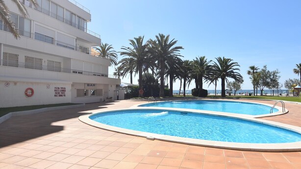 Una piscina amb un solàrium enrajolat, un bar i un edifici amb balcons.
