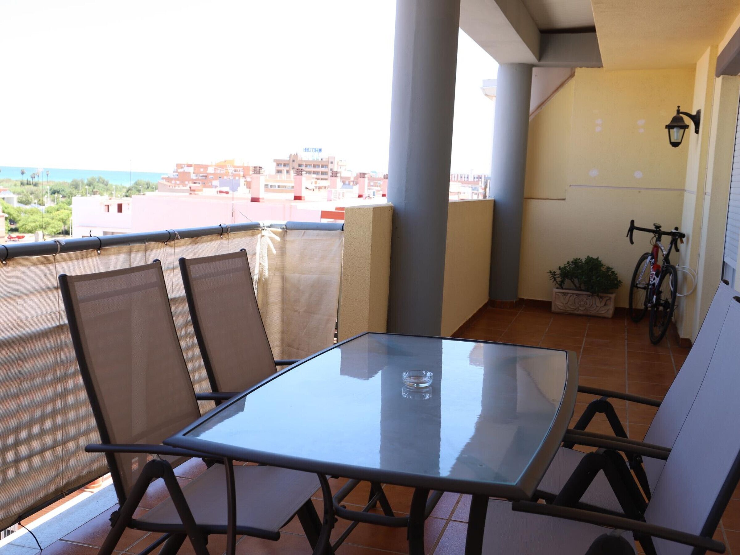Een balkon met een glazen tafel en stoelen, een potplant en een fiets.