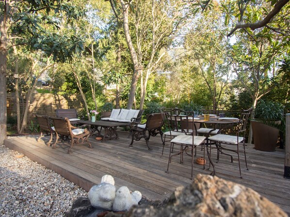 Un patio al aire libre con una terraza de madera, una mesa redonda y varias sillas.