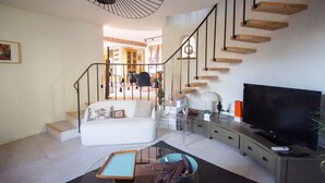 A living room with a sofa, a coffee table, a TV, and a staircase. - Carqueiranne: Charming Villa with Pool, Sea View, for 8 Guests (Carqueiranne)