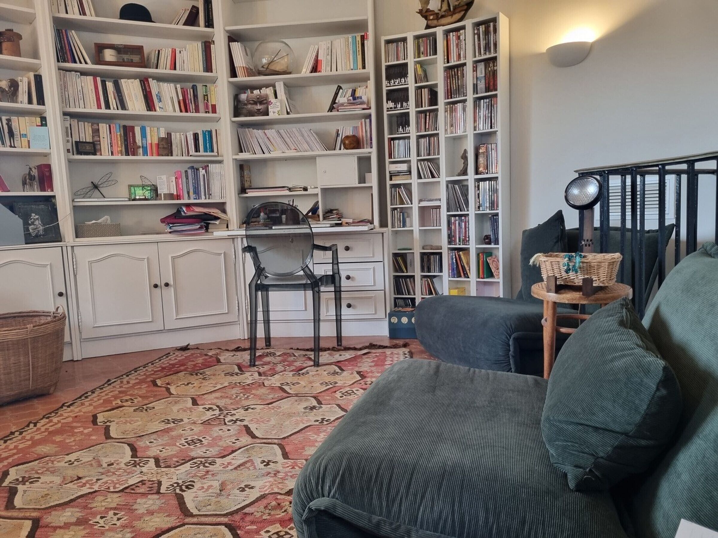 A living room with a sofa, a small table with a basket, and a bookshelf filled with books and decorative items.