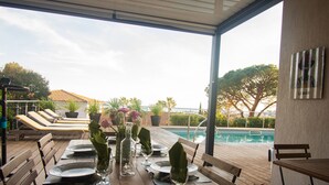 A wooden deck with a pool table set up for dining, overlooking a swimming pool. - Carqueiranne: Charming Villa with Pool, Sea View, for 8 Guests (Carqueiranne)