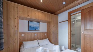 Dormitorio con paneles de madera, una cama, toallas, un cuadro enmarcado y zona de ducha.