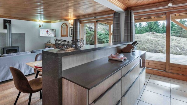 Una cocina moderna con una isla central, techo de madera y ventanas amplias con vistas al exterior.