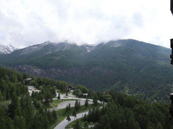 Un paysage montagneux avec une route sinueuse, des bâtiments et une zone boisée.