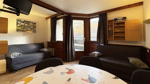 A cozy room with two dark sofas, a small table with a colorful tablecloth, a flat-screen TV mounted on the wall, and a bookshelf. - Spacious studio 6 ppl, ski-in/ski-out, Free Wifi (Les Orres)