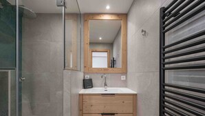 A modern bathroom with a glass shower enclosure, a wooden vanity with a sink, and a towel rack.