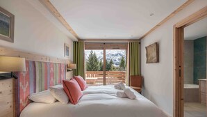 A bedroom with a large bed, wooden headboard, and a view of a balcony with a wooden railing.