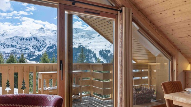 A wooden balcony with a glass door, offering a view of snow-covered mountains.