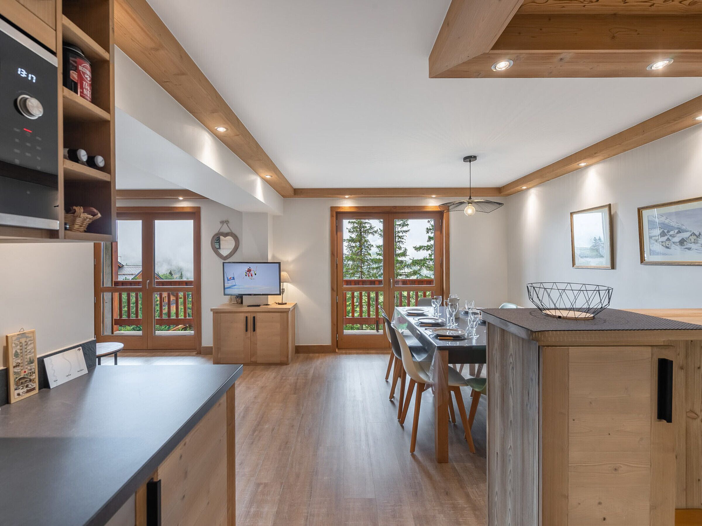 Una cocina moderna con armarios de madera, una zona de comedor con mesa y sillas, y un televisor sobre un mueble.