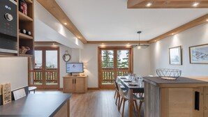 Una cocina moderna con armarios de madera, una zona de comedor con mesa y sillas, y un televisor sobre un mueble.