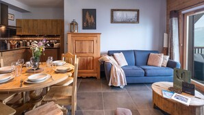 Un salon moderne comprenant un coin repas, des meubles en bois, un canapé bleu et une grande fenêtre donnant sur un paysage.