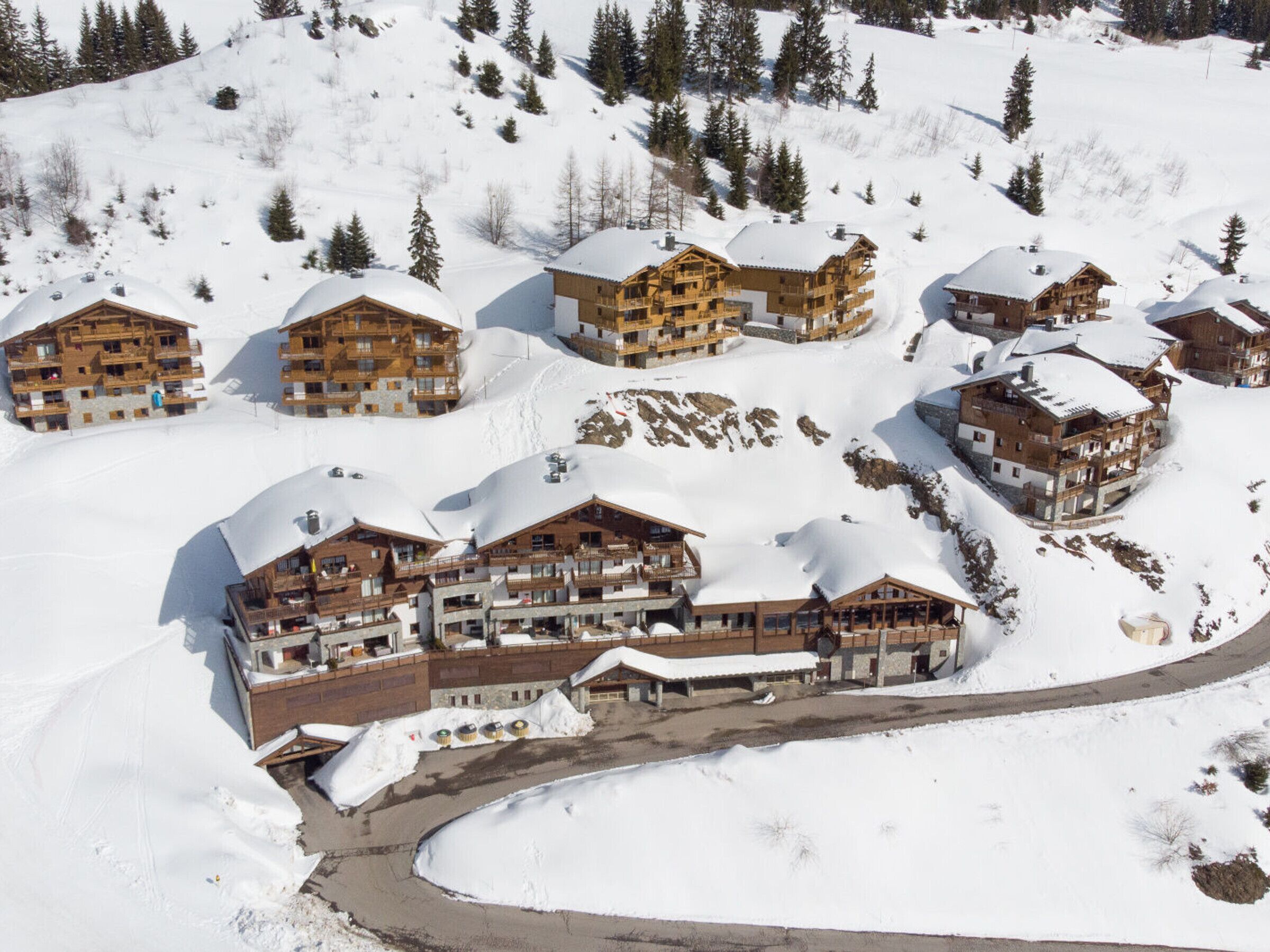 A snow-covered ski resort with multiple wooden buildings, including a large lodge with balconies and a ski lift visible.