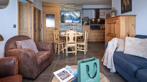 A living room with a brown leather sofa, a blue sofa, a dining table with chairs, and a kitchen area with wooden cabinets and a stone backsplash. - Beautiful apartment in Bisanne 1500 with parking for 6 people (Villard-sur-Doron)