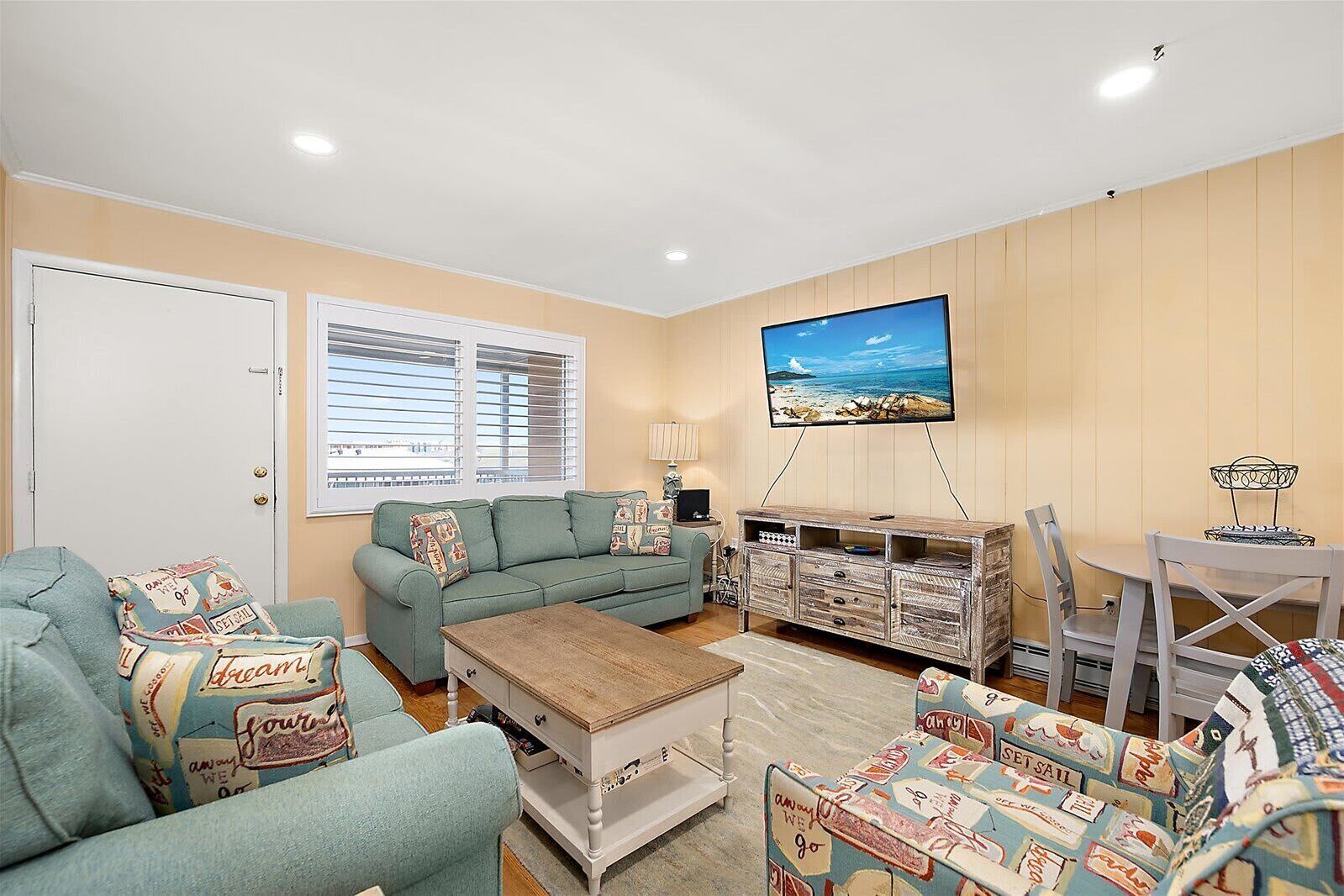 A living room with a sofa, a coffee table, a TV mounted on the wall, and a dining area with a table and chairs.