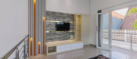 A modern living room with a flat-screen TV, built-in shelves, and a glass door leading to a balcony.