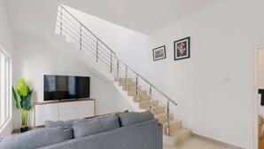 Een moderne woonkamer met een grijze bank, een flatscreen-tv, een trap en twee ingekaderde foto's aan de muur.