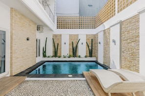 A swimming pool with a pebble-lined deck, surrounded by walls with a brick pattern and vertical stone accents. - Gloen Villa by Betterplace (Canggu)