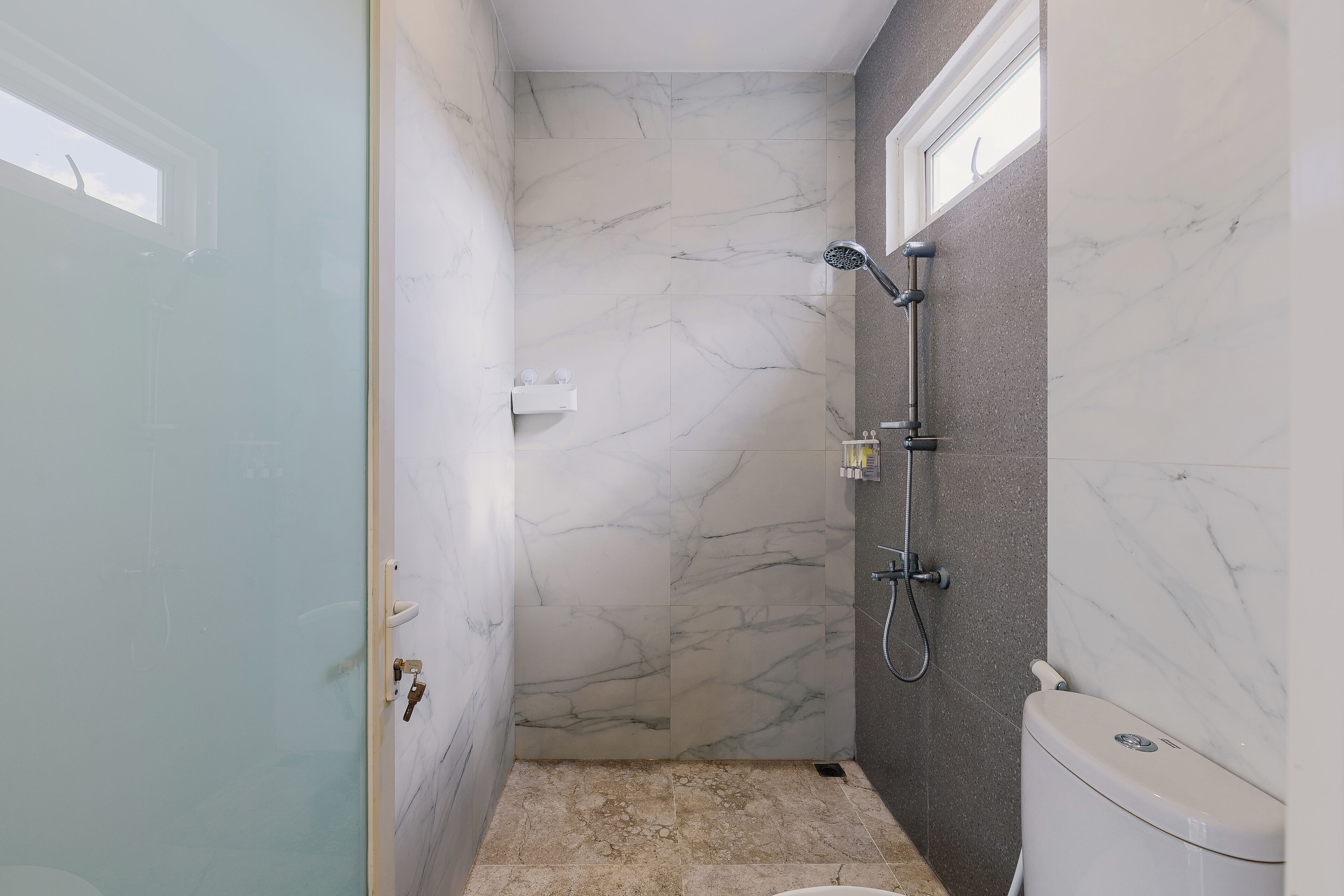 A bathroom with a marble shower wall, a toilet, and a sink.