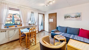 Una sala de estar acogedora con un sofá, una mesa de comedor con sillas, una mesita con un adorno y un cuadro en la pared.