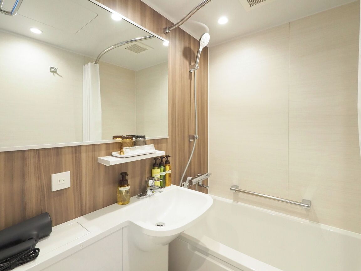 A modern bathroom with a white sink, a mirror, a shower, and a wooden vanity.