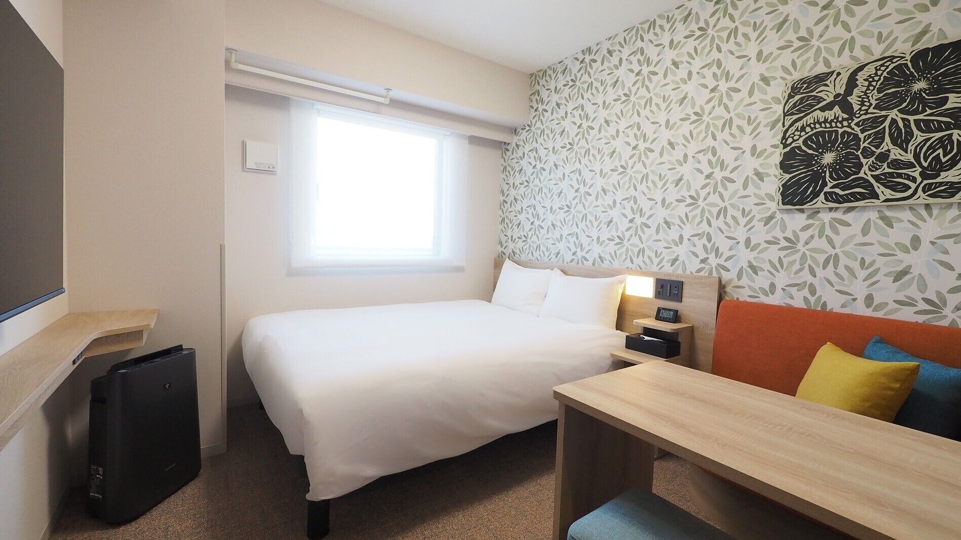Una habitación de hotel con cama, mesita de noche y ventana.