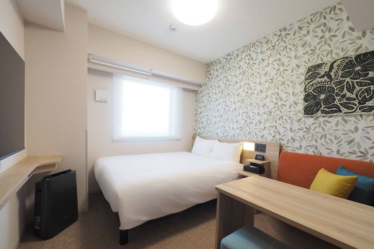 Habitación de hotel con cama, escritorio, silla, televisor, ventana y pared con diseño.