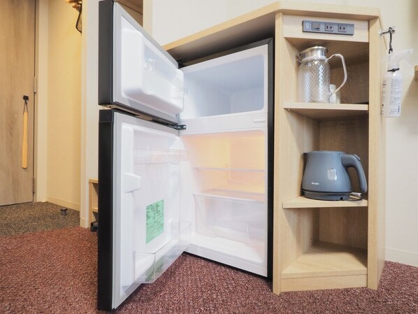 Un refrigerador compacto con compartimento congelador, tetera integrada y un estante con un recipiente de vidrio.